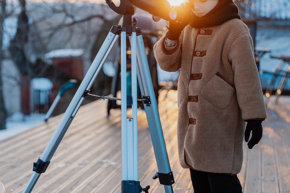 Débutant observant le ciel étoilé avec des jumelles et un télescope installés dans un jardin.